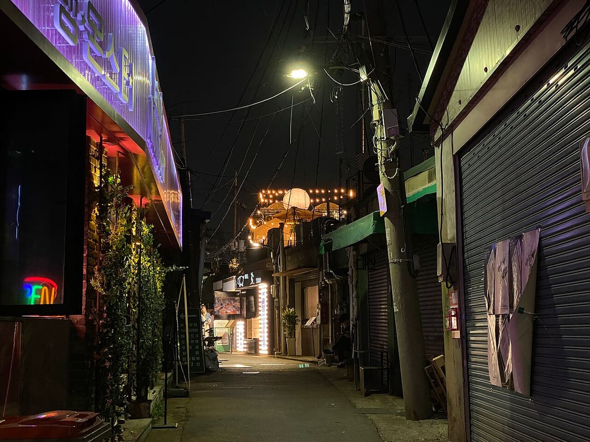 A Mullae alley at night, with a neon-signed bar next to shuttered metal workshops.