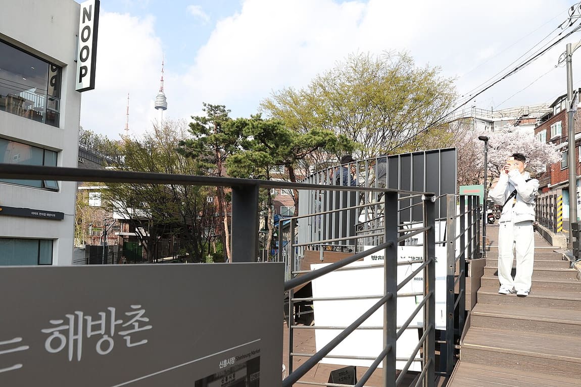 A Haebangchon signboard with N Seoul Tower and cherry blossom behind it.