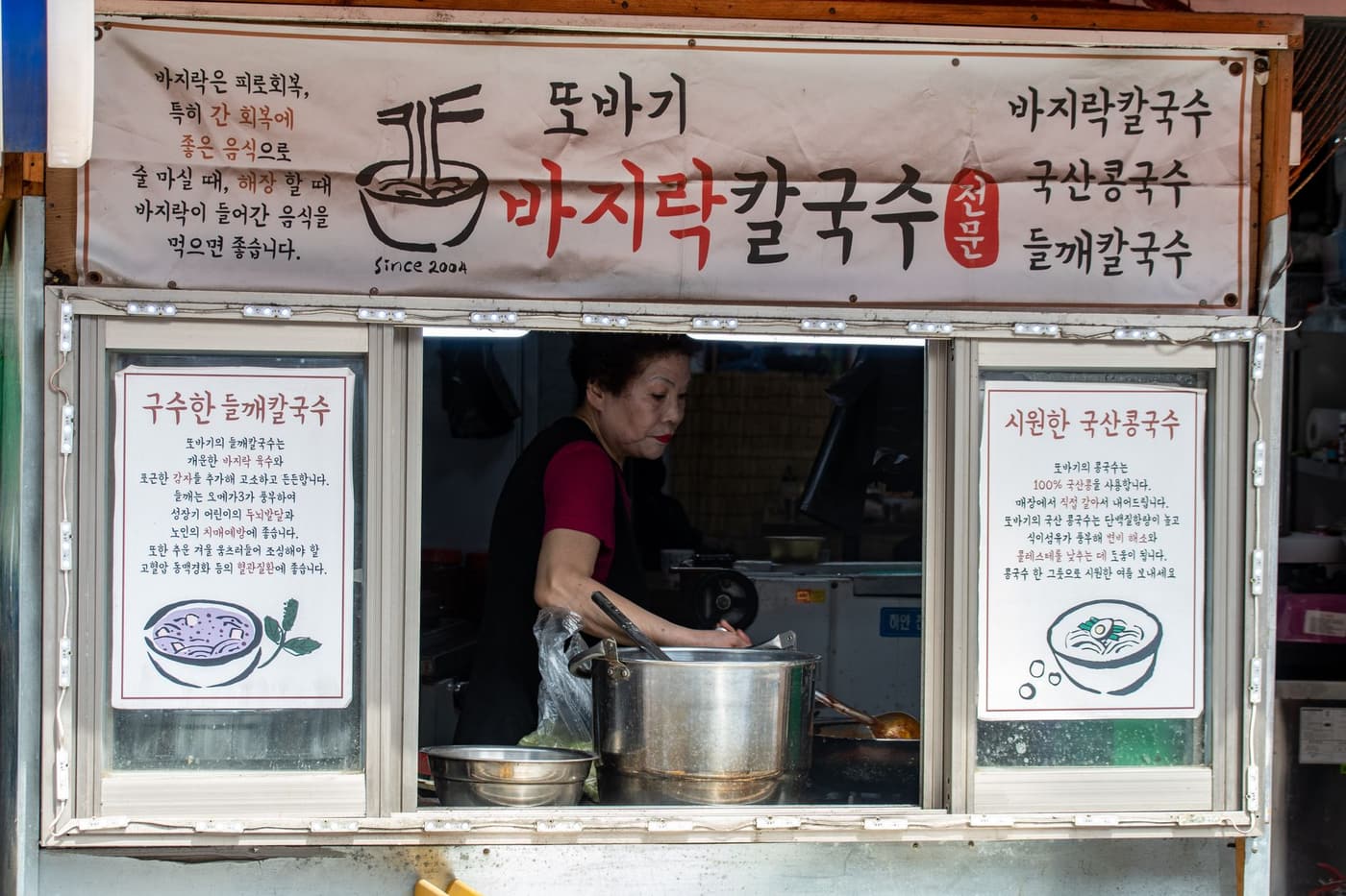 A street vendor preparing traditional Korean noodles at a food stall.