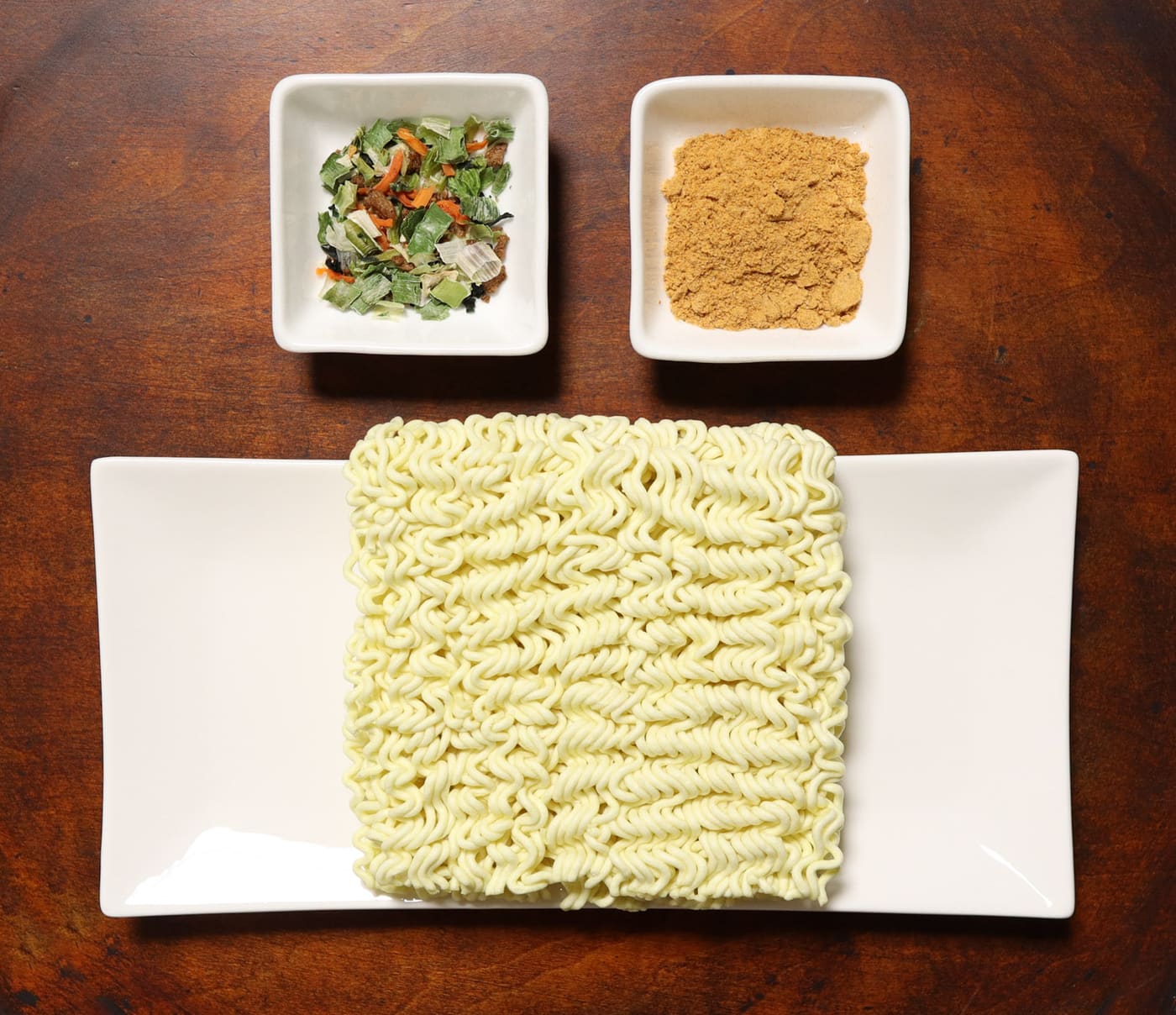 Contents of a Jin Ramen mild packet: noodle block, dried vegetable flake, and a pale tan soup powder.