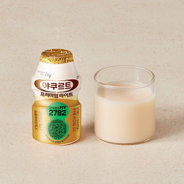A bottle of 야쿠르트 프리미엄 라이트 next to a glass of the milky-white drink.