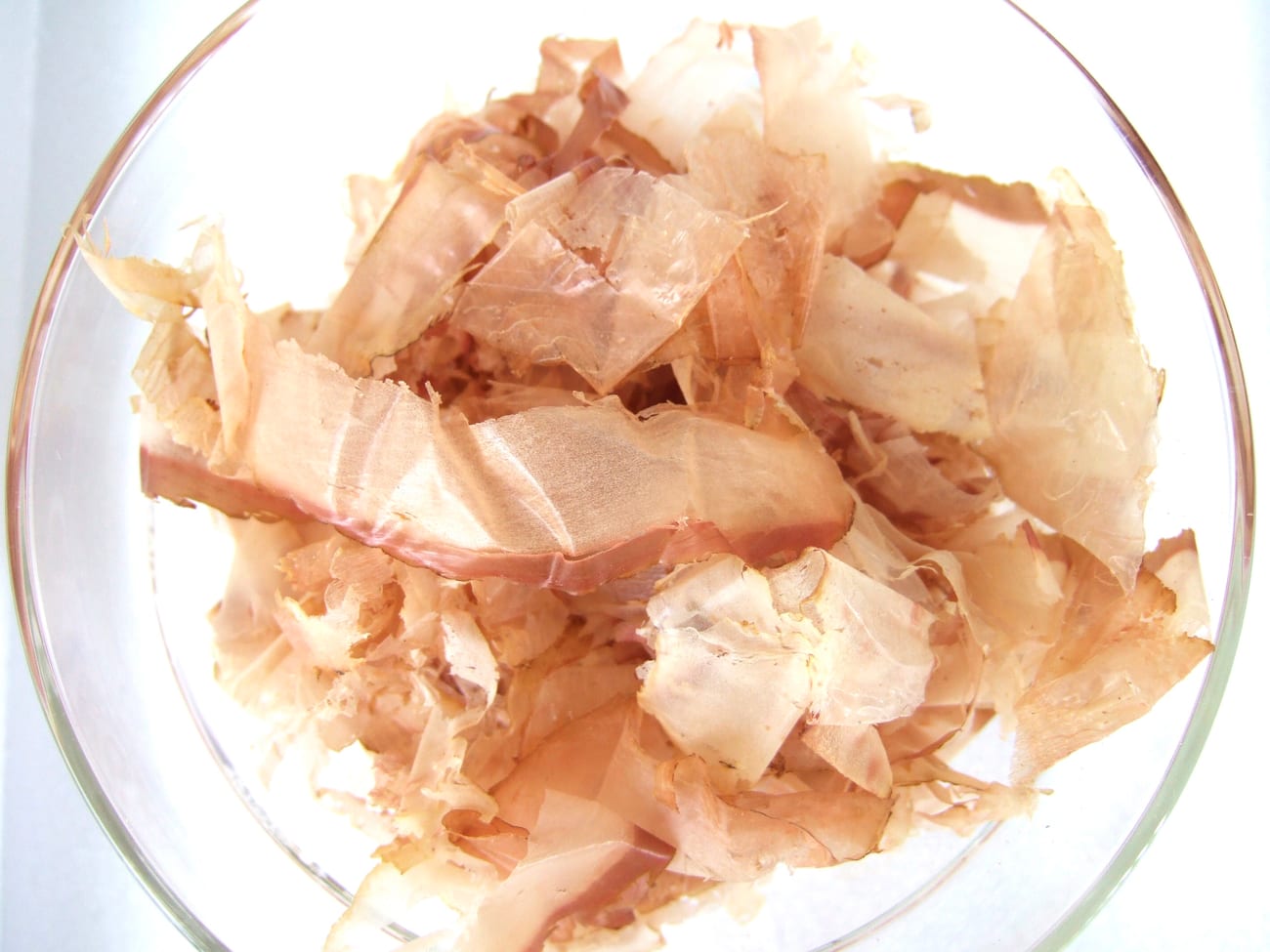 Dried bonito flakes, pale pink and paper-thin, heaped in a pile.