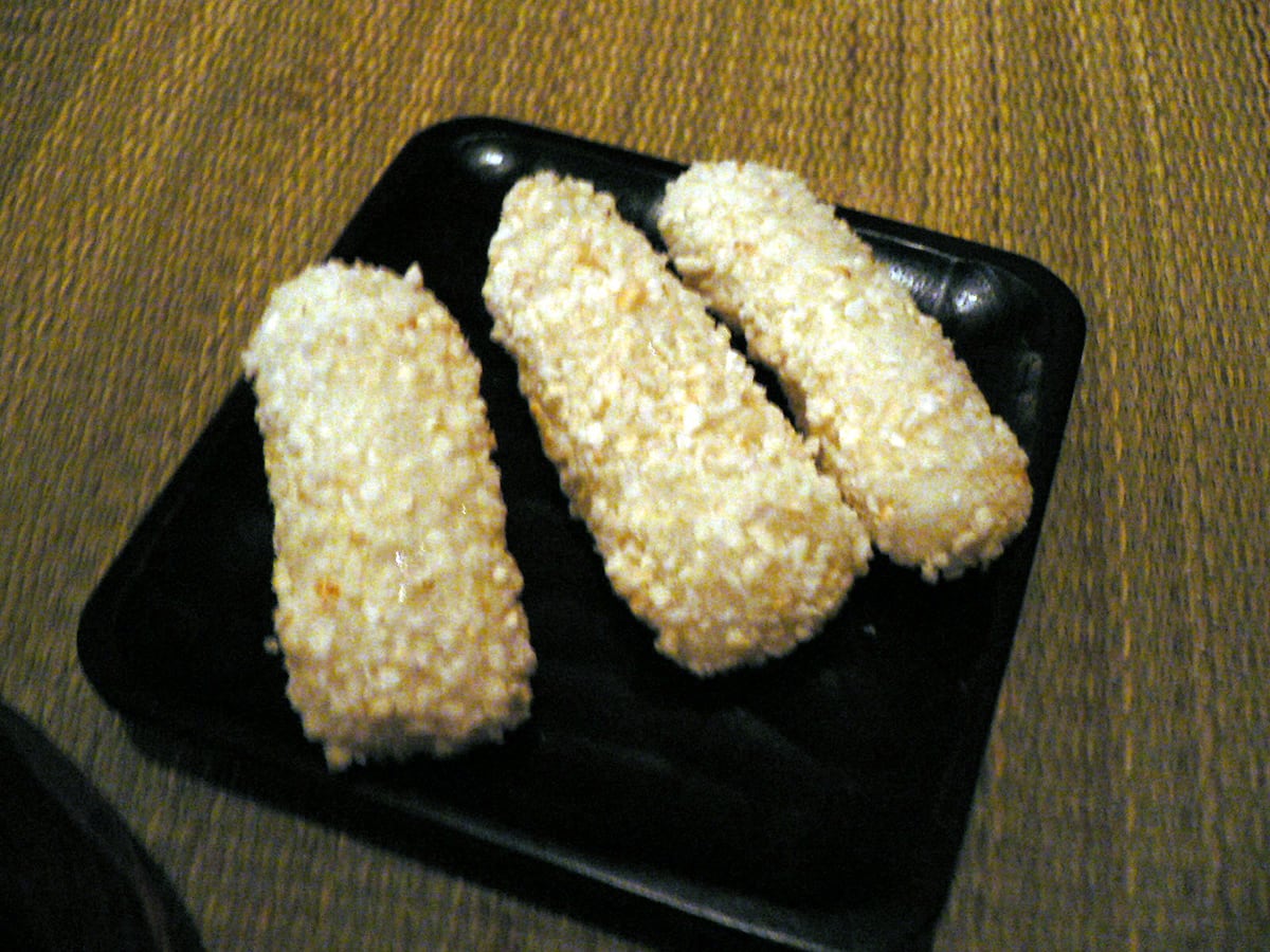 Yugwa — pale Korean traditional sweets coated in puffed rice, served on a black dish.
