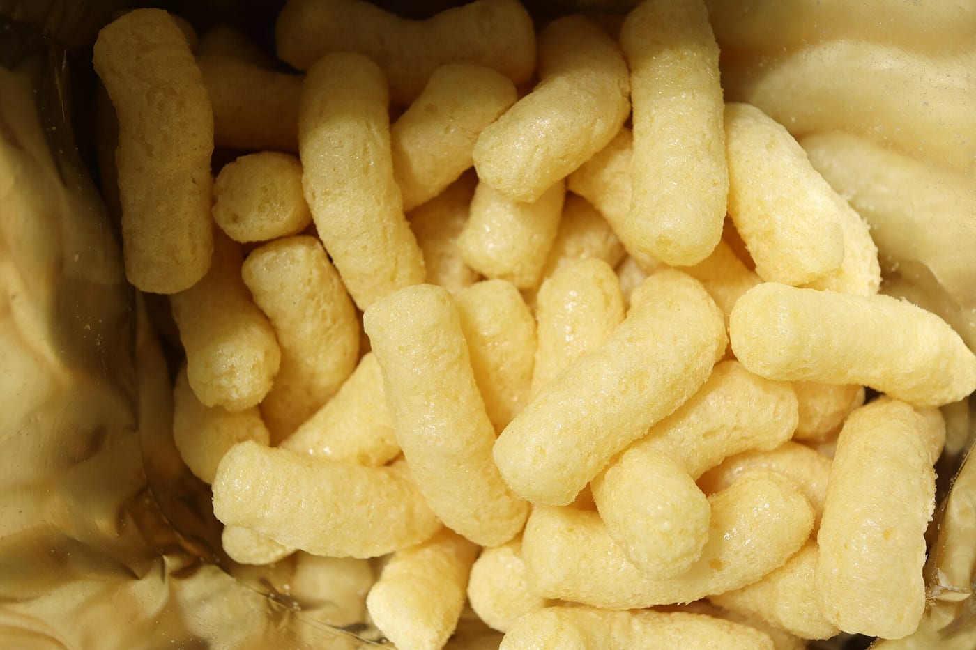 Pale banana-shaped corn puffs filling the inside of an opened foil bag, seen from above.
