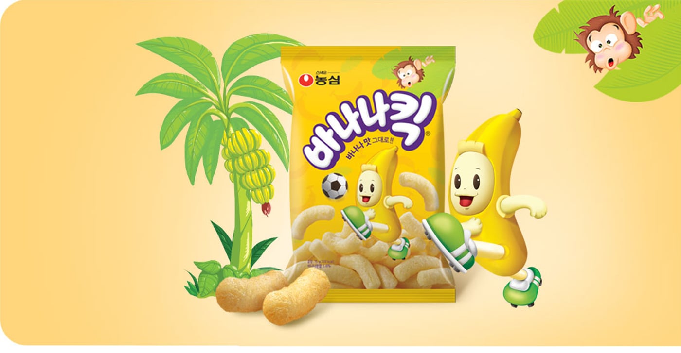 Nongshim Banana Kick packaging artwork — a yellow bag with cartoon banana characters, beside loose pale corn puffs shaped like small bananas.