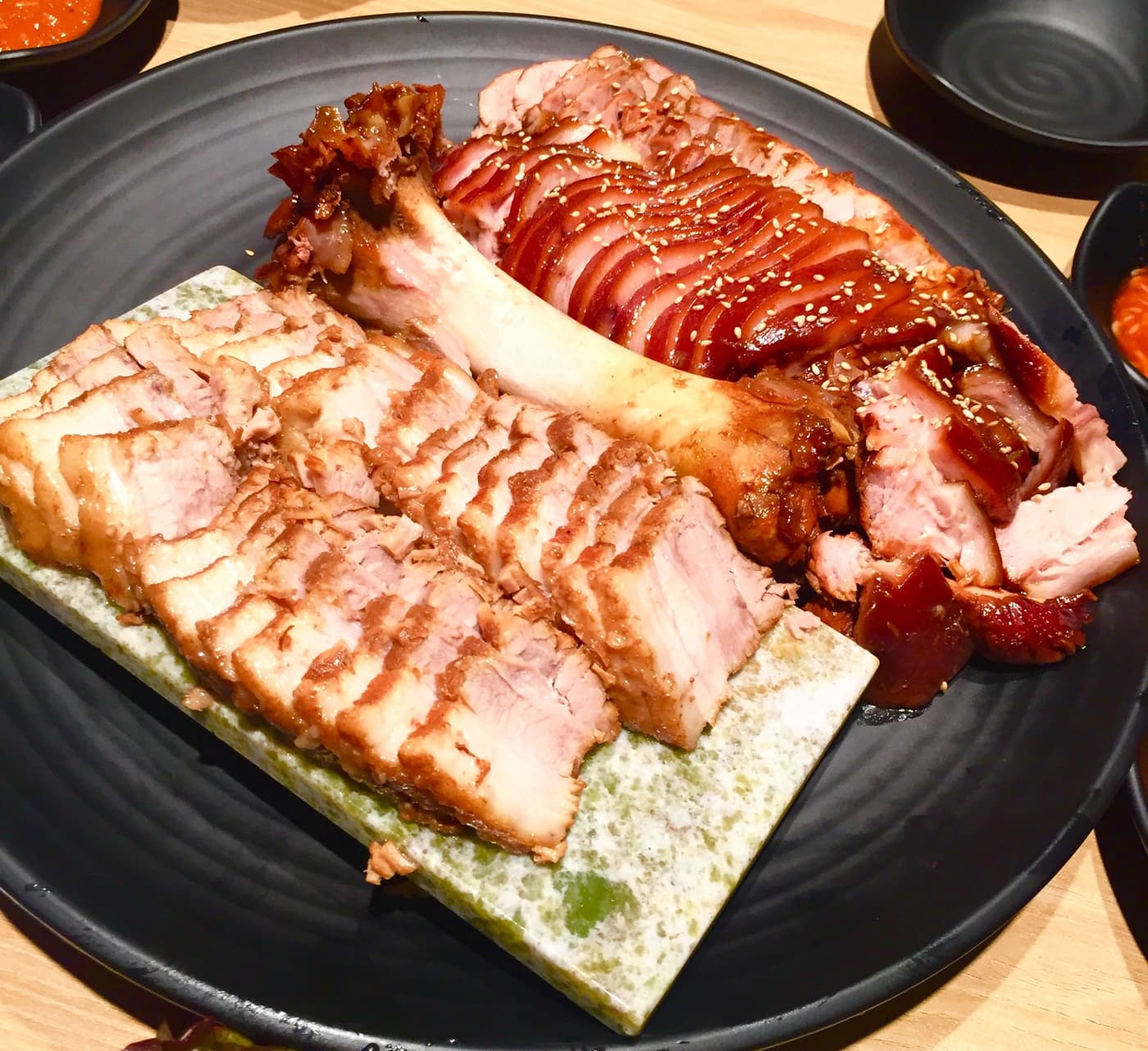 A single plate holding both dishes: pale sliced boiled pork belly on the left, glossy dark soy-braised trotter with the bone still in on the right.