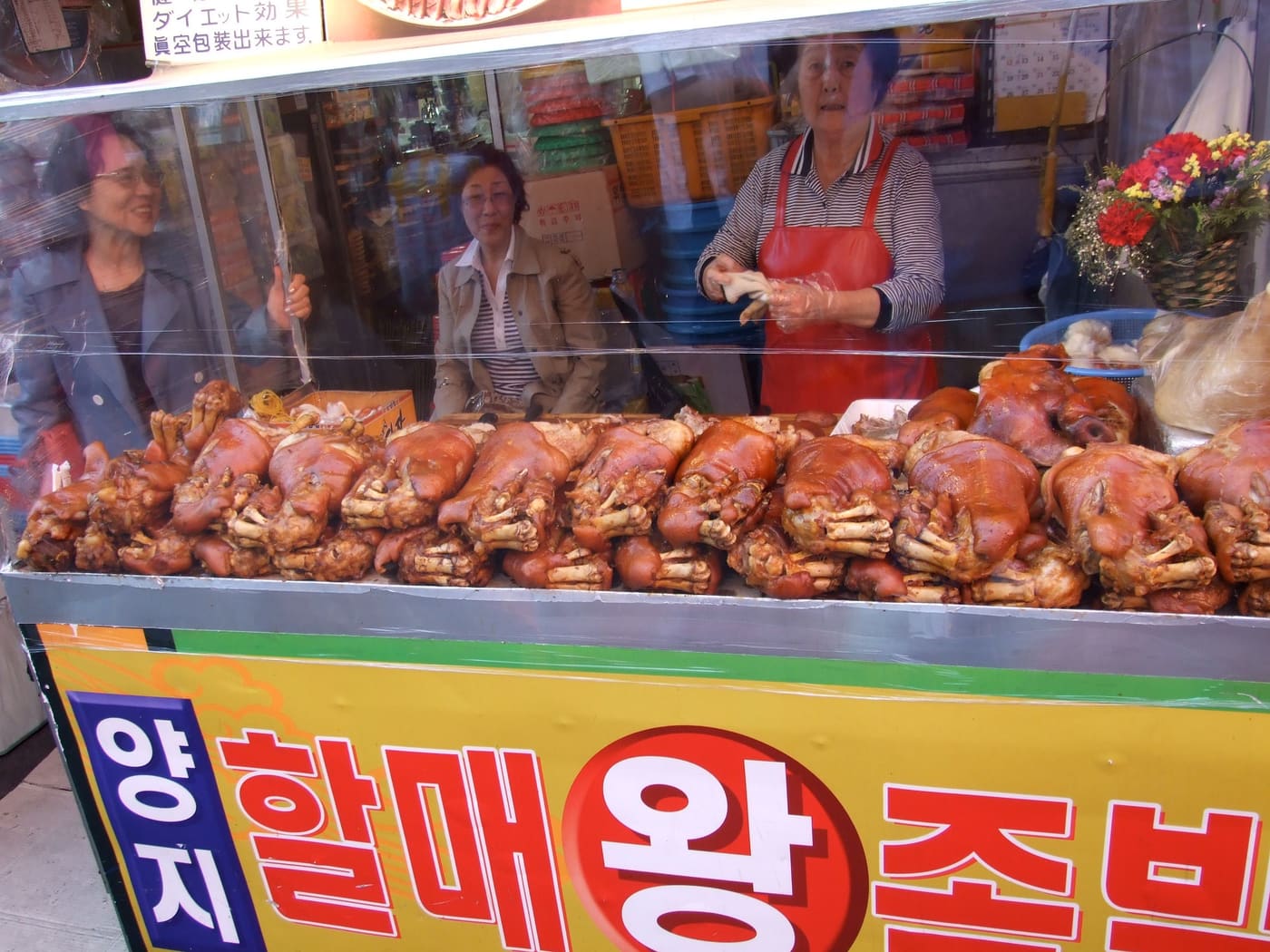 A market stall with whole braised trotters stacked under glass and a Korean sign reading 왕족발.