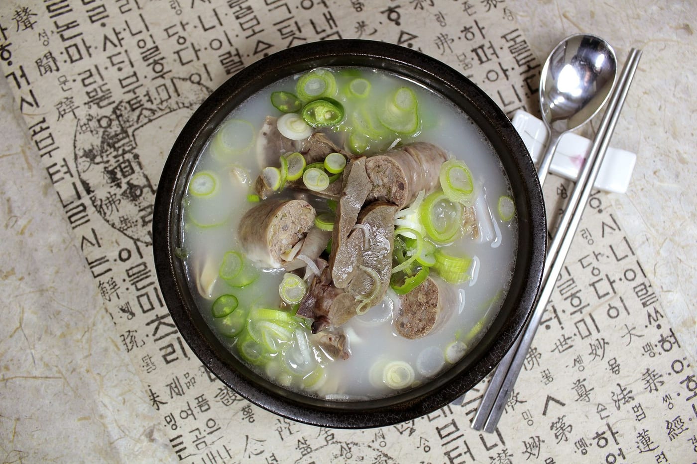 A bowl of Korean haejangguk hangover soup, a dark broth thick with vegetables and meat, served in a stone bowl with side dishes.