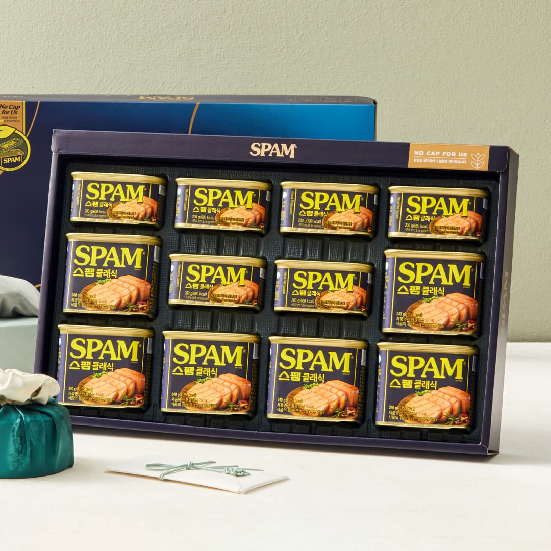 A navy Spam gift box holding twelve cans in two visibly different sizes — a row of small 200g cans at the top and larger 340g cans below.