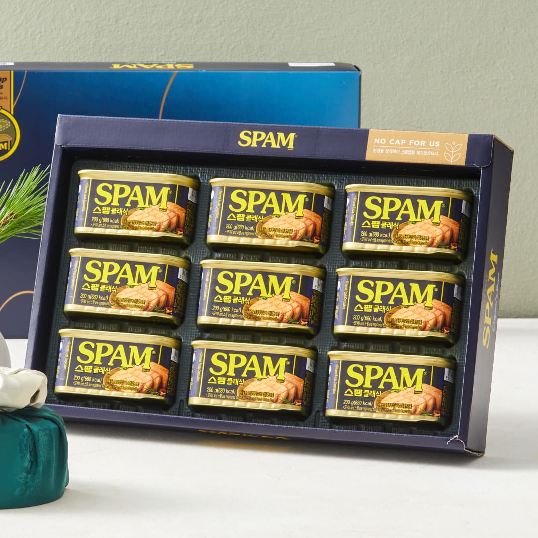 A navy Spam gift box with nine 200g cans arranged in three rows of three, a pine sprig visible at the left edge.
