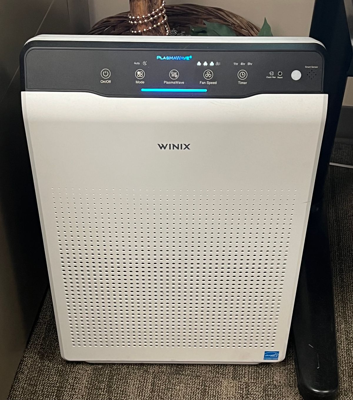 A Winix 5500-2 air purifier standing in a home, its control panel lit and the PlasmaWave button visible.