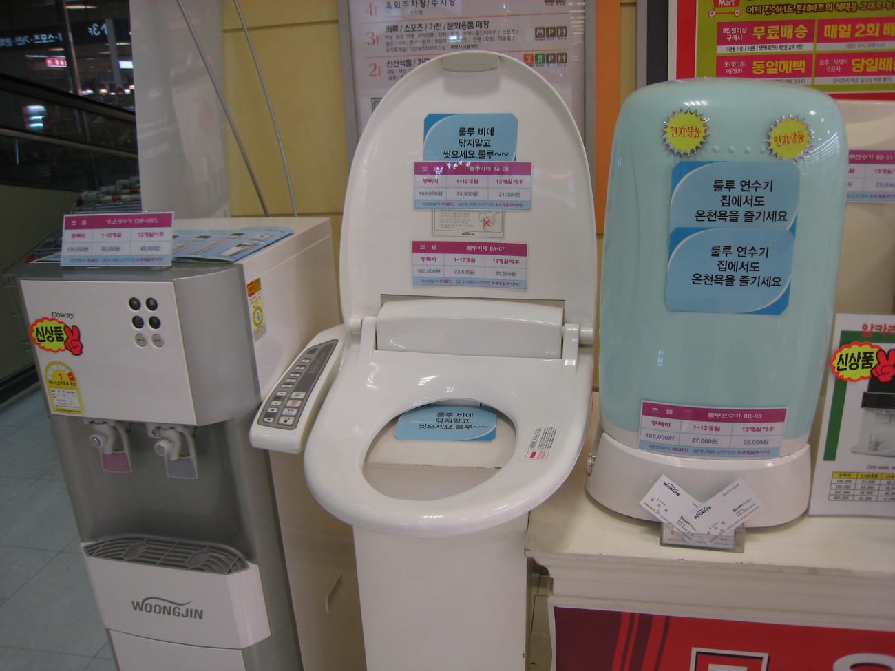 A Seoul appliance shop display in 2007 with a Woongjin water purifier, an electronic bidet seat and a water softener standing side by side under Korean promotional signage.