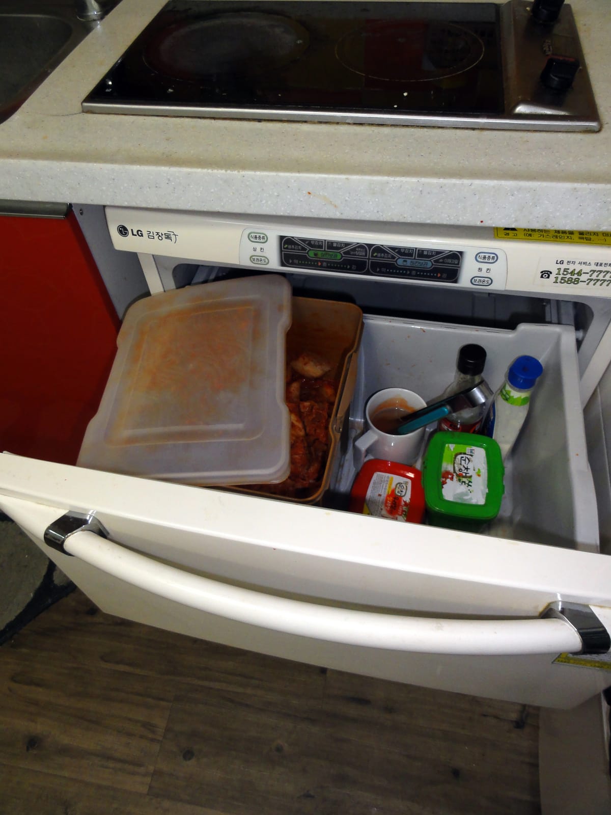 An LG stand-type kimchi refrigerator with its lower drawer pulled out, holding sealed containers of kimchi and side dishes.