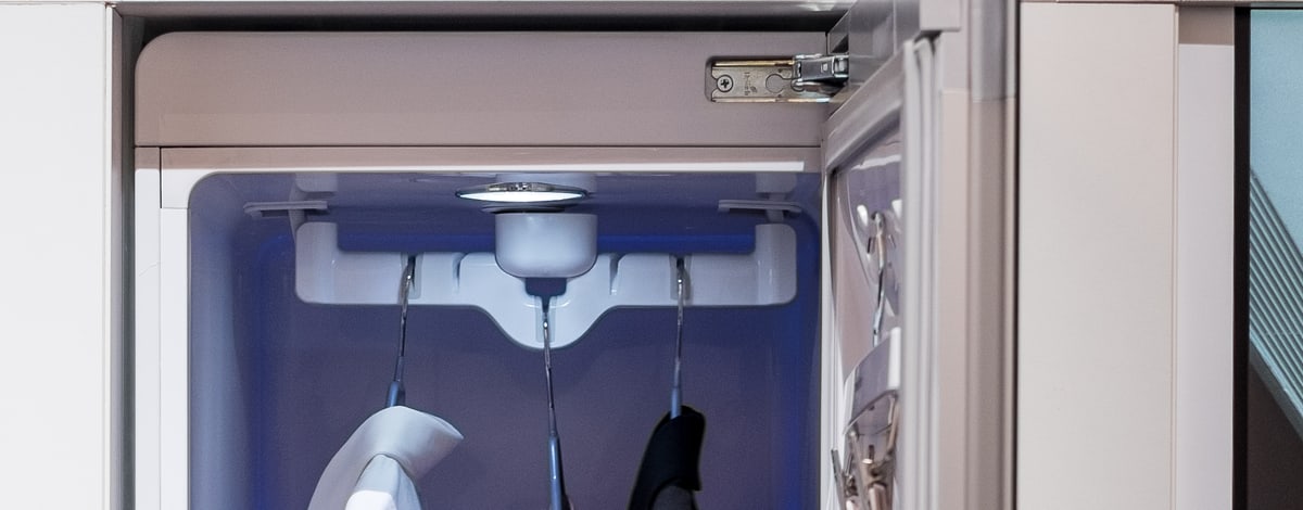 Close-up of the Styler's ceiling-mounted moving hanger rack, three hanger slots clipped into a white swinging bar with a lit steam vent behind.