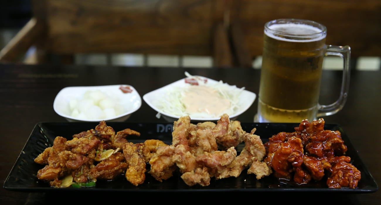 A plate of Korean fried chicken with pickled radish, salad and a glass of beer at a Korean restaurant table.