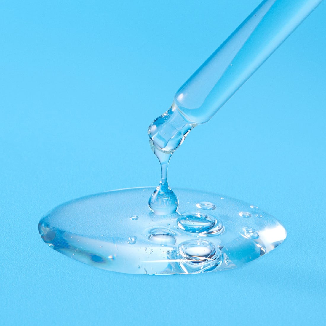 A dropper releasing a drop of clear serum onto a small pool of the fluid, against a blue background.
