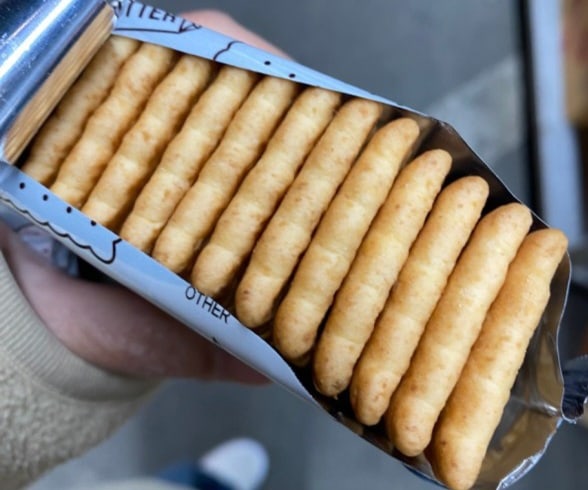 Open packet of 빠다코코낫 showing the ridged rectangular butter biscuits stacked upright inside the foil sleeve.