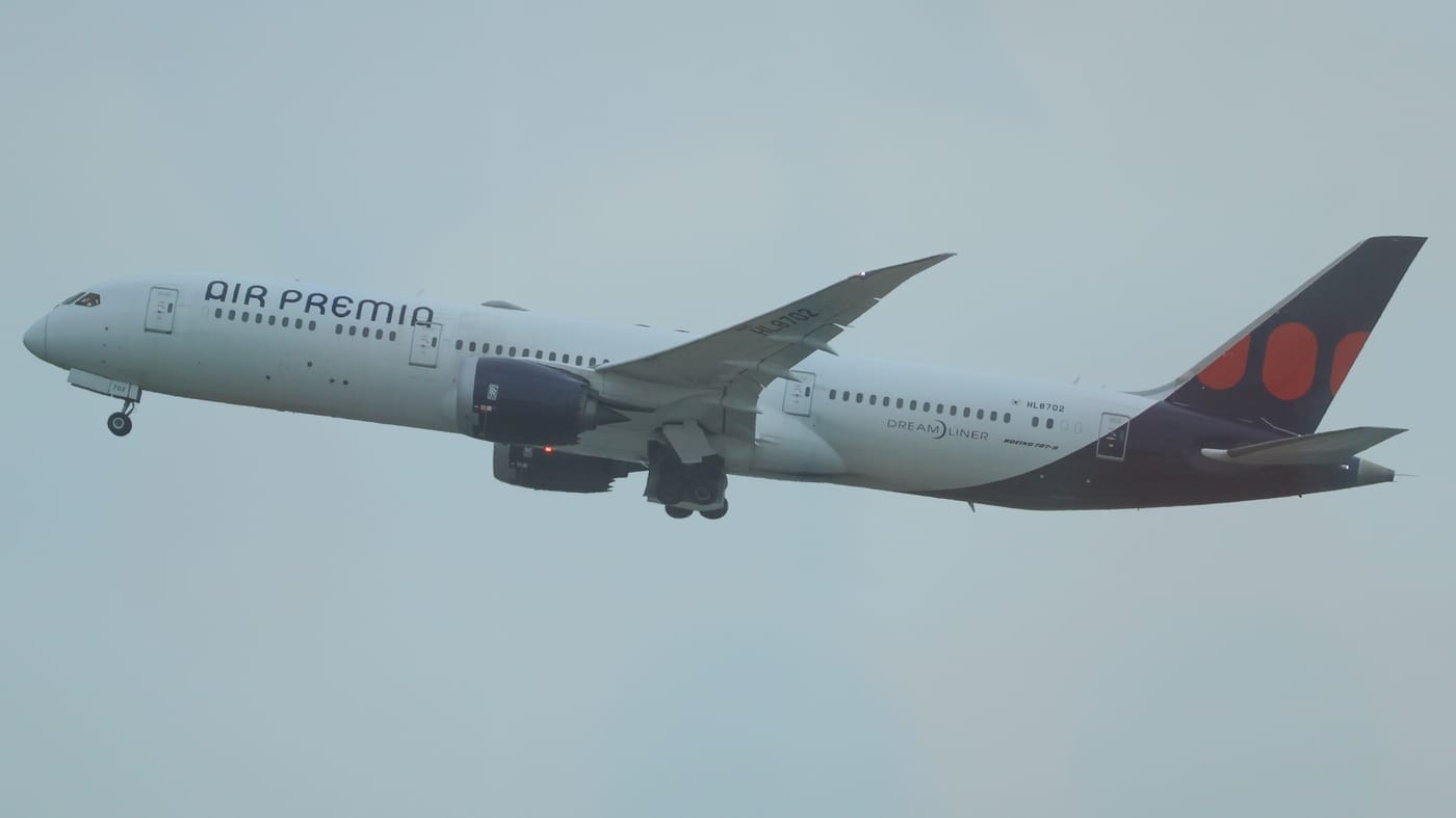 An Air Premia Boeing 787-9 climbing away from Incheon Airport with its landing gear still extended, white fuselage with AIR PREMIA titles and a dark tail marked with two red discs.