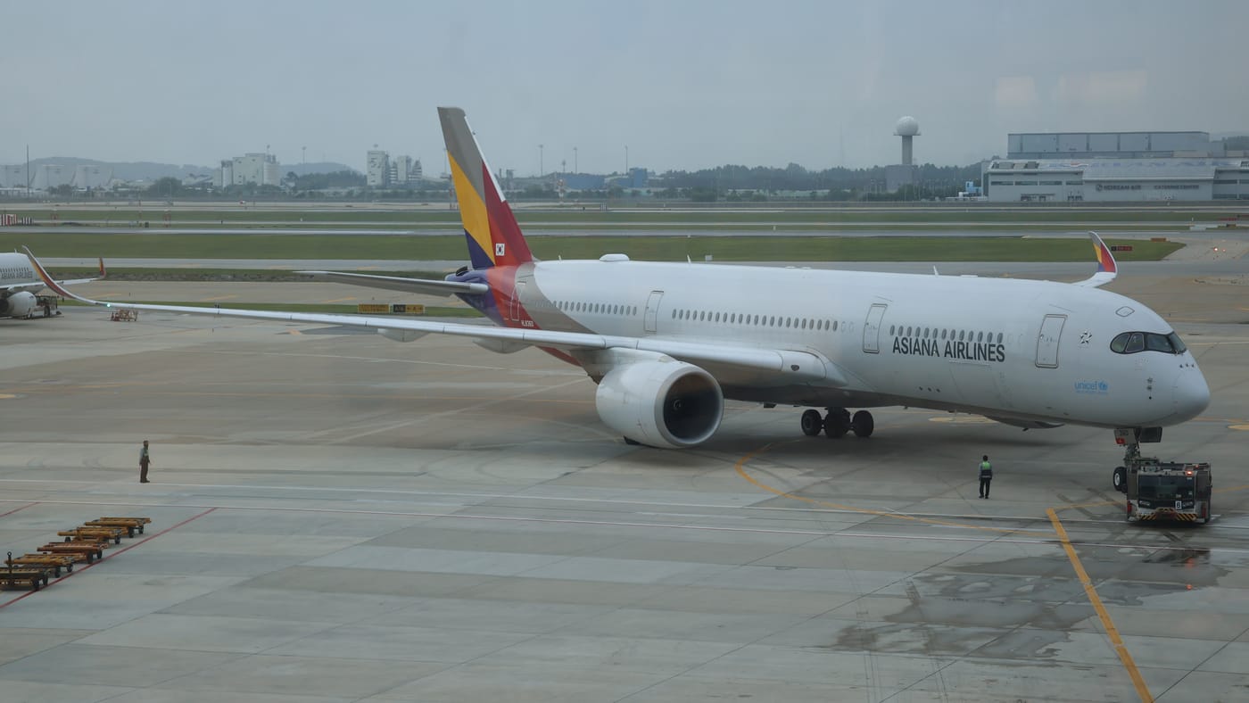 An Asiana Airlines Airbus A350 parked on stand at Incheon Airport with ground crew alongside, white fuselage with ASIANA AIRLINES titles and the multicoloured striped tail.