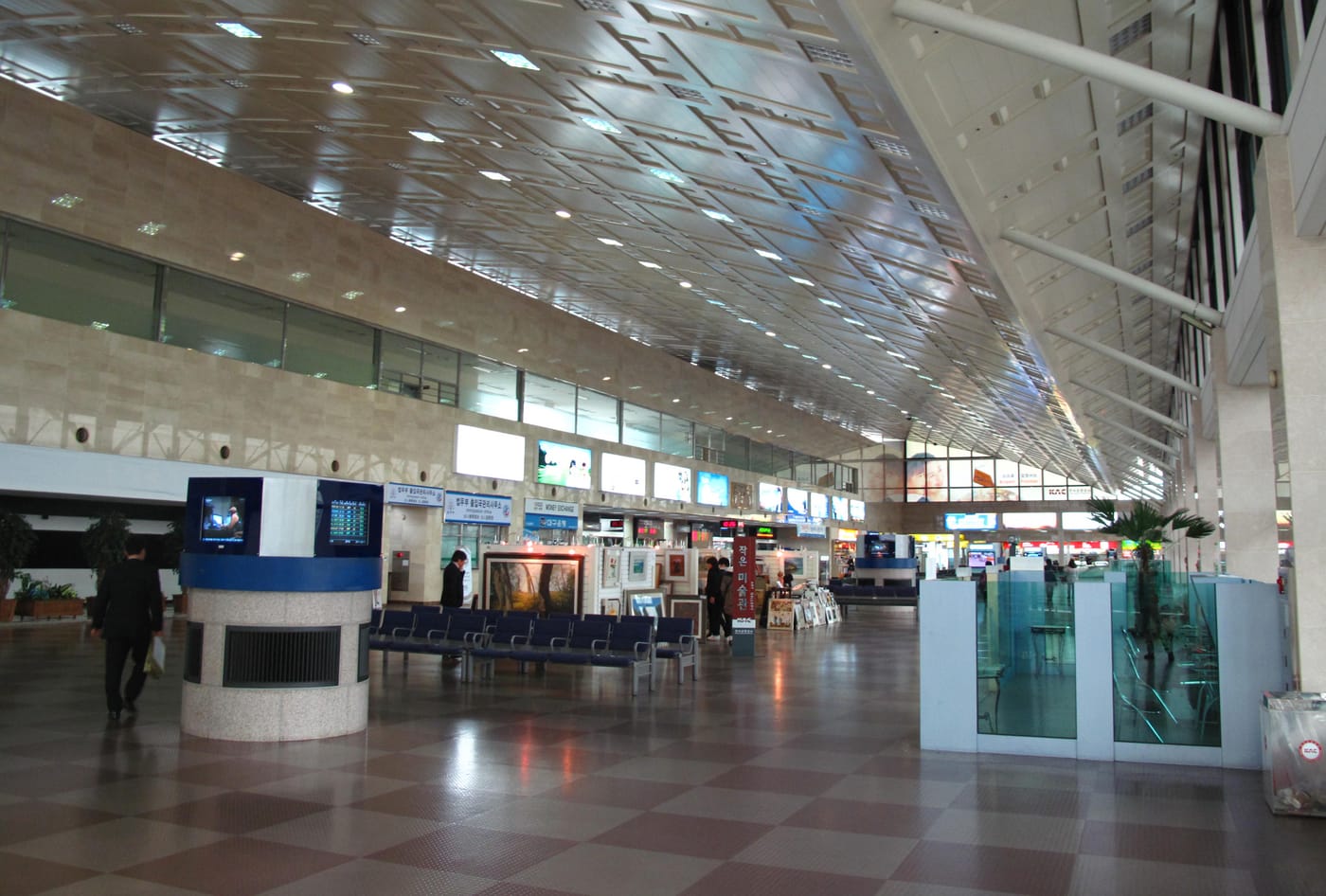The interior of Daegu International Airport, a small stone-and-glass terminal hall with rows of empty seating and a handful of people walking through.