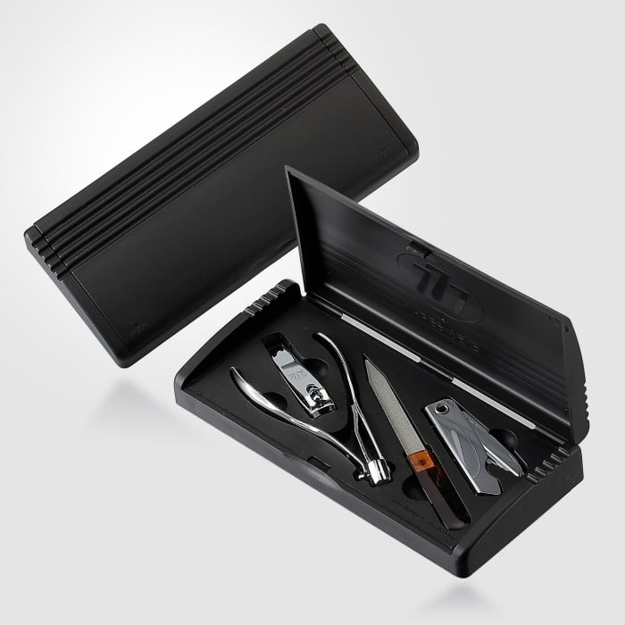 An open black hard-case Three Seven grooming set showing a nail clipper, a cuticle nipper, a nail file and a folding tool seated in moulded slots.
