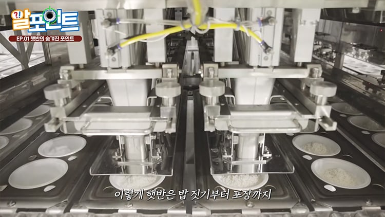 A Hetbahn filling line inside a CJ plant, with stainless dosing heads above a conveyor of empty bowls, some already filled with rice, from CJ's own factory video.