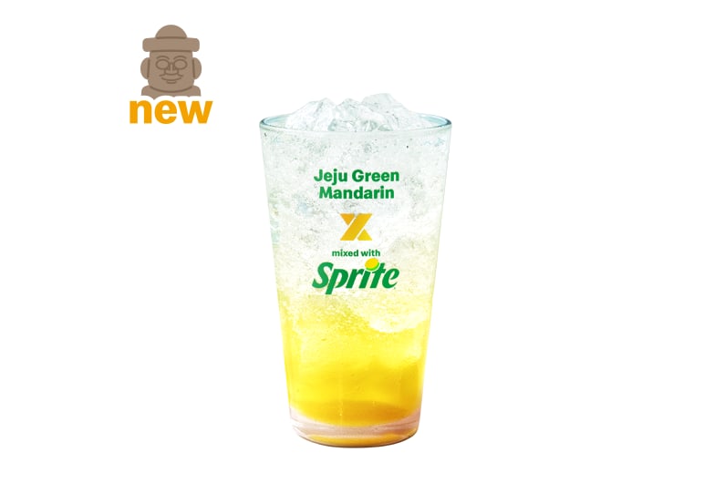 The Jeju Green Tangerine McFizz, a tall clear cup of pale green sparkling drink with ice and a slice of green citrus, on a white background.