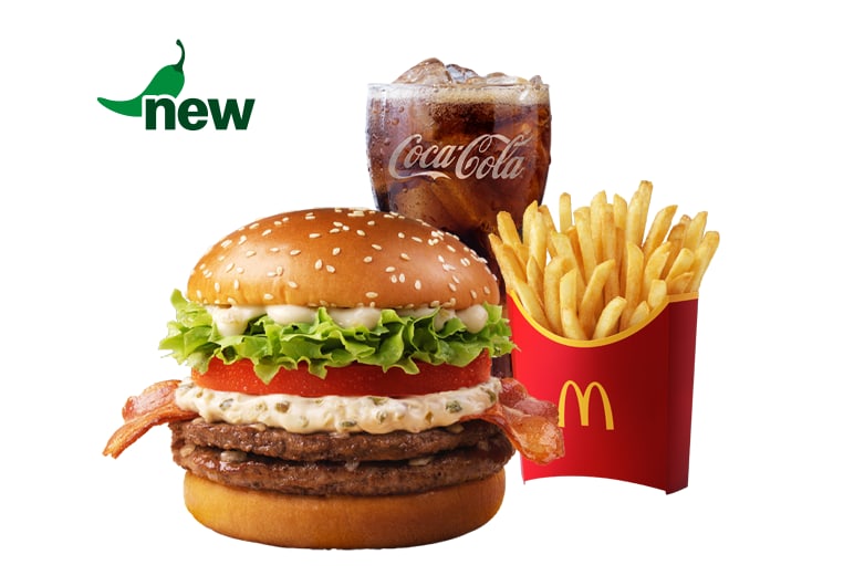 The Jinju Pepper Cream Cheese Beef Burger meal on a white background: a sesame bun with two beef patties, bacon, tomato, lettuce and a pale green-flecked cream cheese sauce, beside fries and a Coca-Cola, with a chilli-shaped NEW badge.