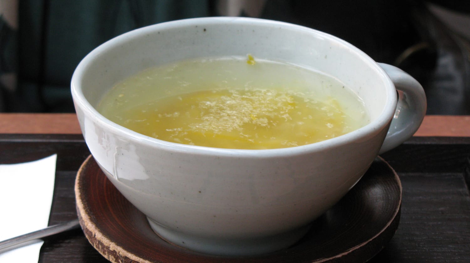 A cup of Korean yuja tea in a ceramic cafe mug, the shredded yellow citrus peel clearly visible suspended in the hot liquid.