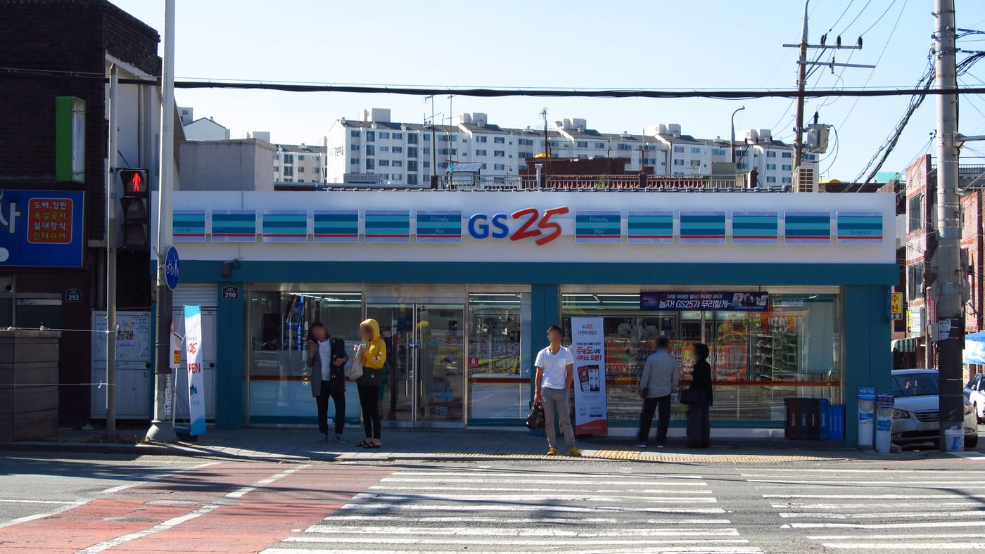 A GS25 convenience store on a Korean street corner in daylight, with the blue-and-white shopfront and residential blocks behind.