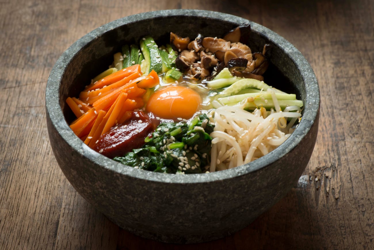 Dolsot bibimbap in a grey stone bowl, with vegetables arranged in sections around a raw egg yolk.