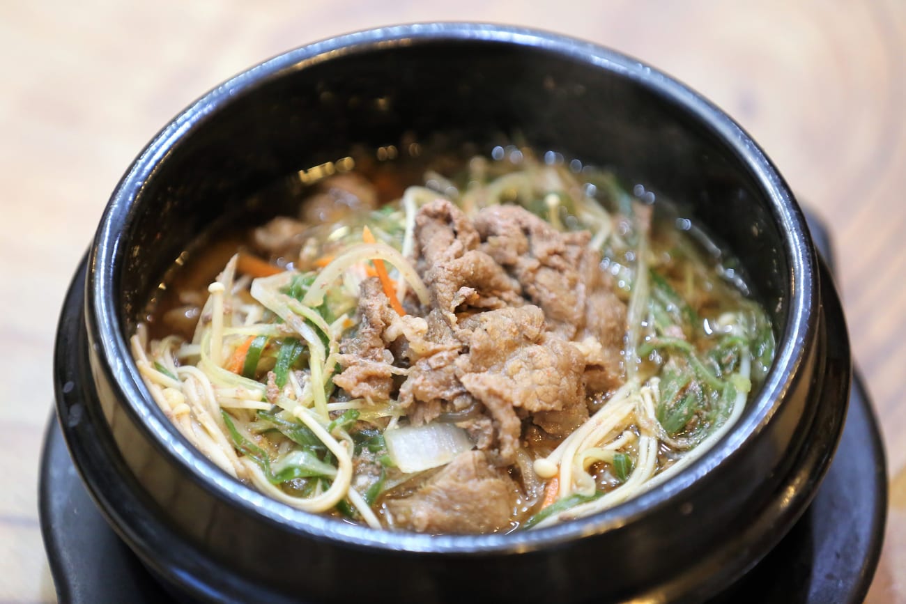 Ttukbaegi bulgogi: thin sliced beef, glass noodles, mushrooms and vegetables in a dark clay pot filled with broth.