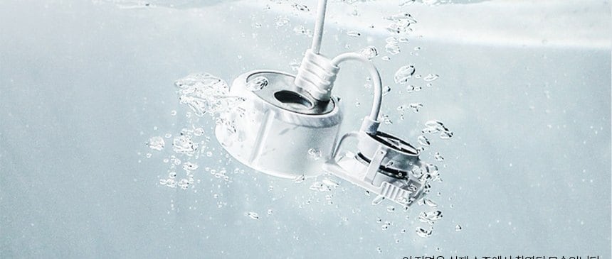 The humidifying engine module of a Korean humidifier photographed fully submerged in water, its power lead coiled beside it and bubbles rising from the transducer housing.