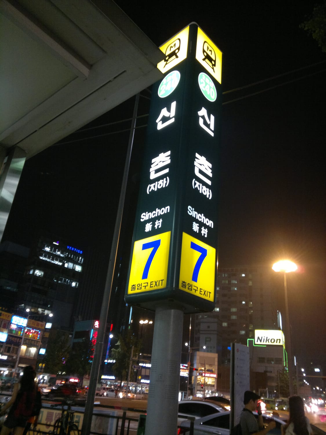 The Sinchon station exit sign at night, with the station name in Korean, English and Chinese and the exit number 7.