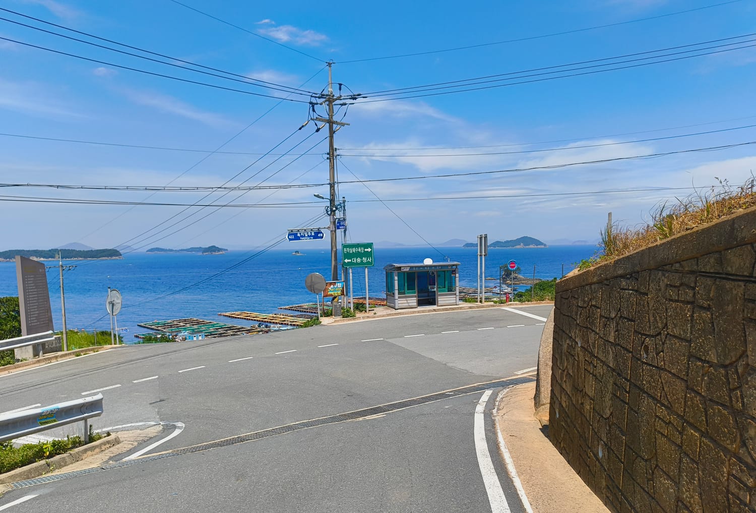 A rural bus stop on a coastal road on Yokjido island, empty road, sea and small islands beyond.