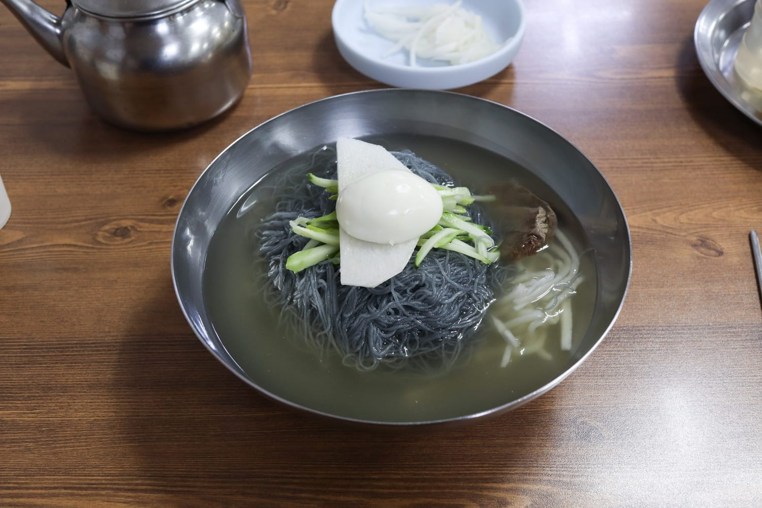A bowl of mul-naengmyeon in Sokcho: dark buckwheat noodles in clear iced broth with cucumber, pear and half an egg.