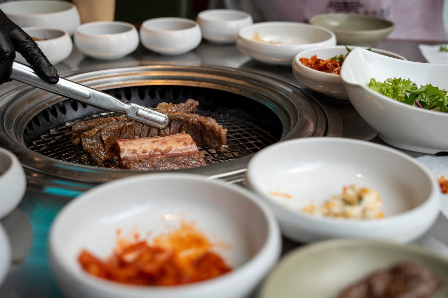 Galbi on a charcoal grill in a Seoul restaurant, tongs and scissors resting over the meat, banchan dishes around the table.