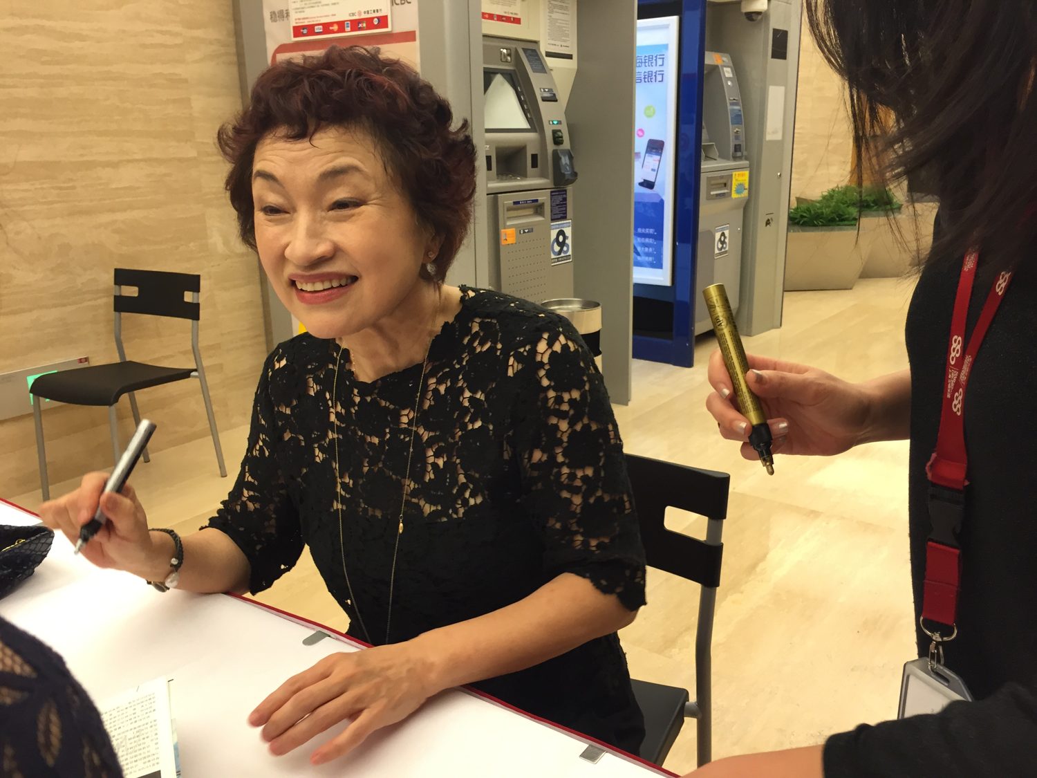 Violinist Kyung-wha Chung, smiling in a black lace top, signing programmes for fans at a table in Singapore.