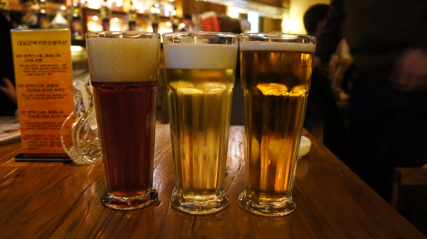 Three glasses of beer, one dark, two pale, on a wooden bar at Taedonggang Microbrewery No. 3 in Pyongyang, 2014.