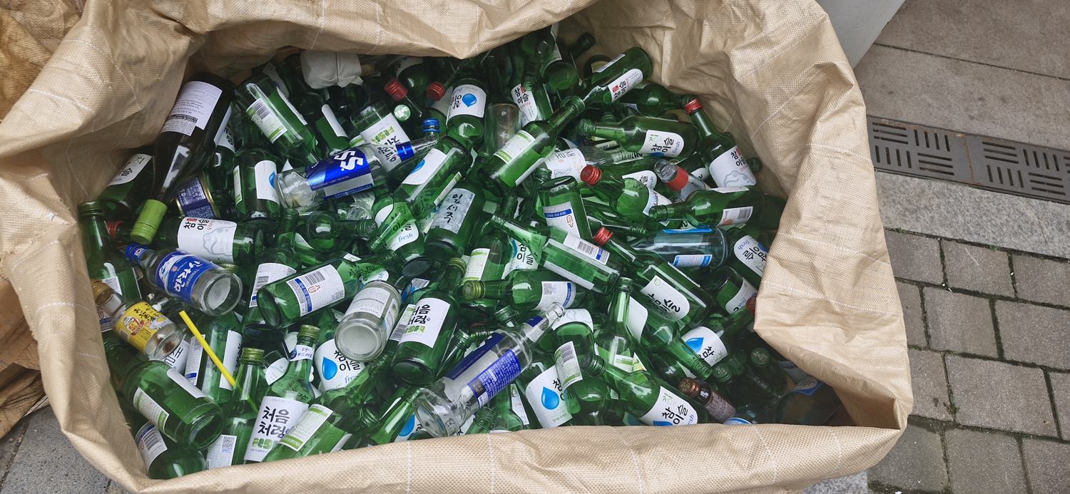 A cardboard box full of empty green soju bottles at an apartment-complex recycling point in Korea.