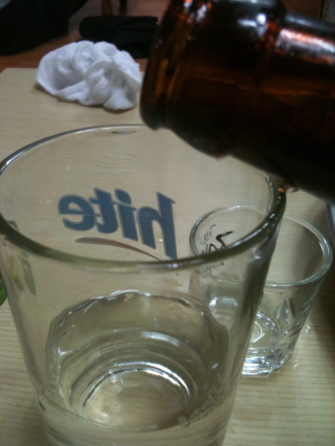 A brown Hite beer bottle being poured into a tall Hite glass to make somaek, a soju glass beside it.