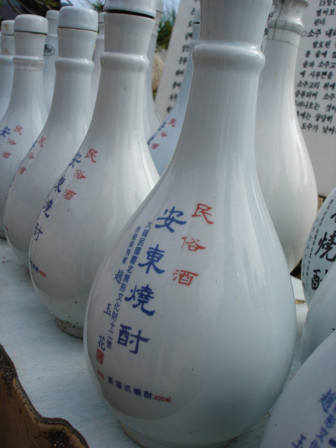 Rows of white ceramic Andong soju bottles with the name in blue and red Chinese characters.