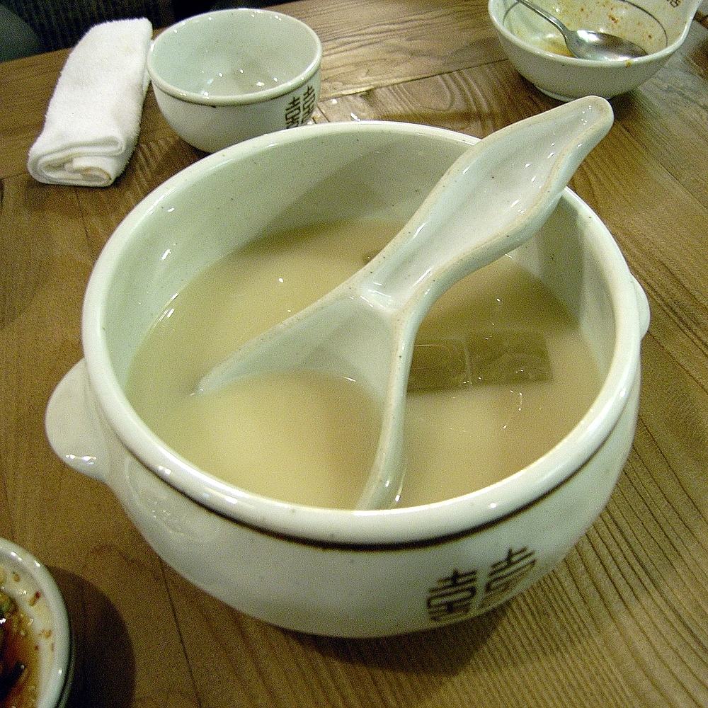 A white ceramic bowl of makgeolli with a ladle, on a wooden table in a Korean restaurant, 2006.