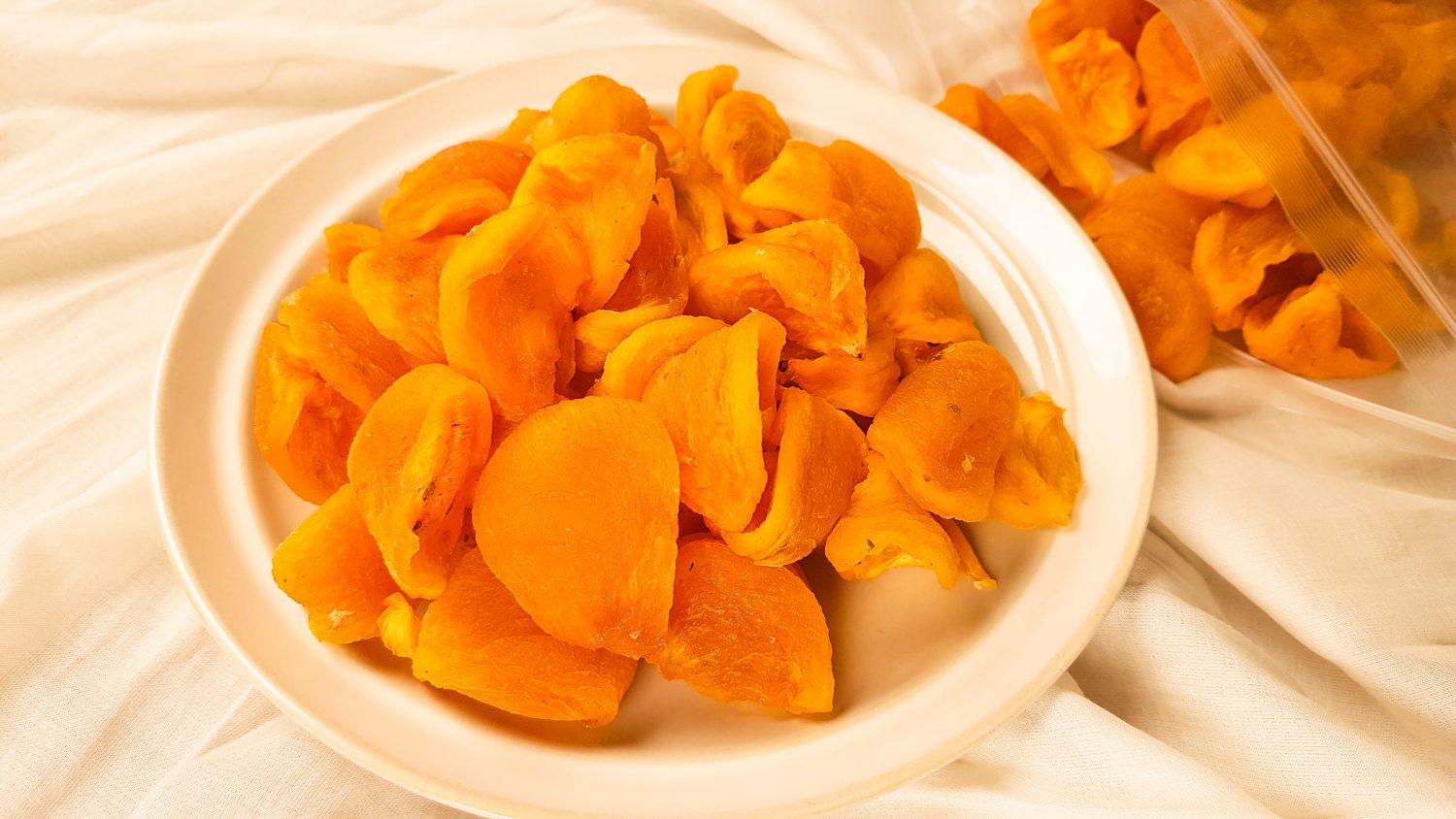 A plate of gotgam, dried persimmons, orange and glossy, on white cloth.