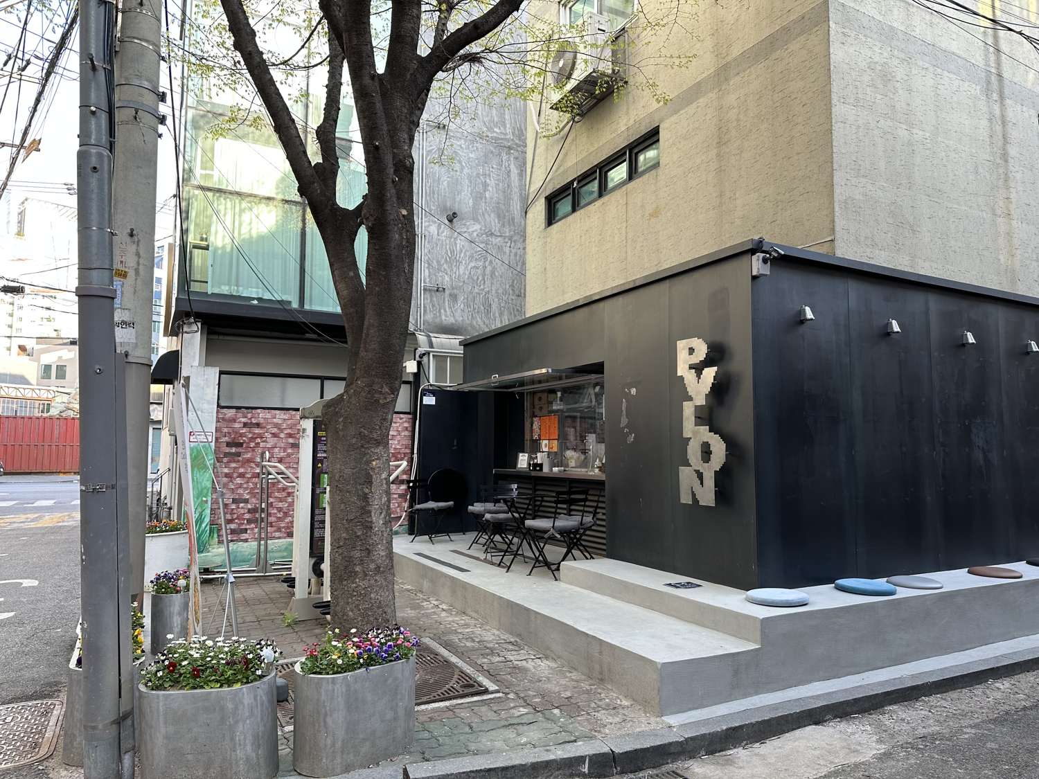 A small black-box café in Seongsu-dong, Seoul, with two outdoor tables under a tree and stone stools on the pavement.