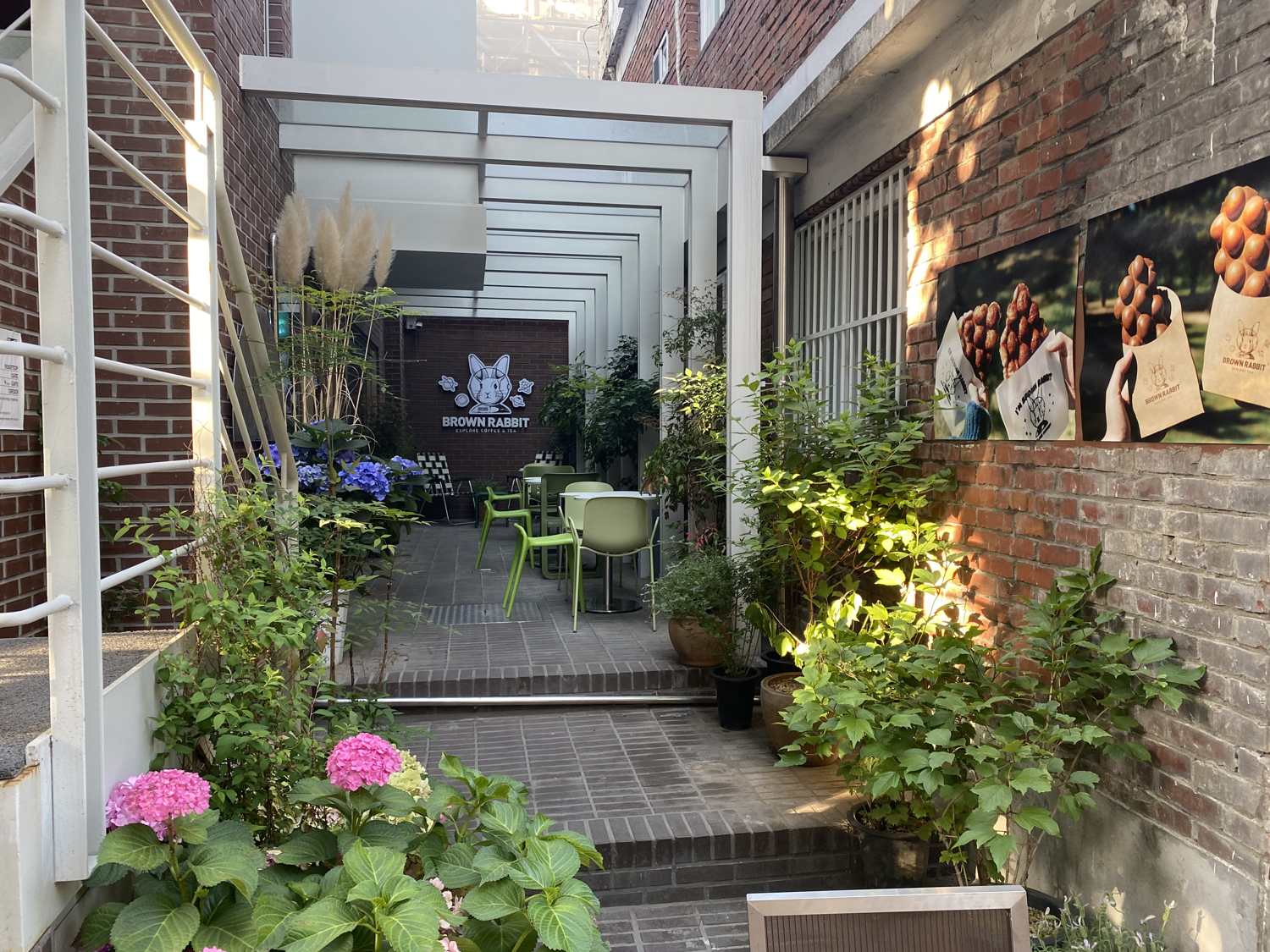 A garden café in Seongsu-dong with hydrangeas, a white pergola and green chairs on a brick terrace.