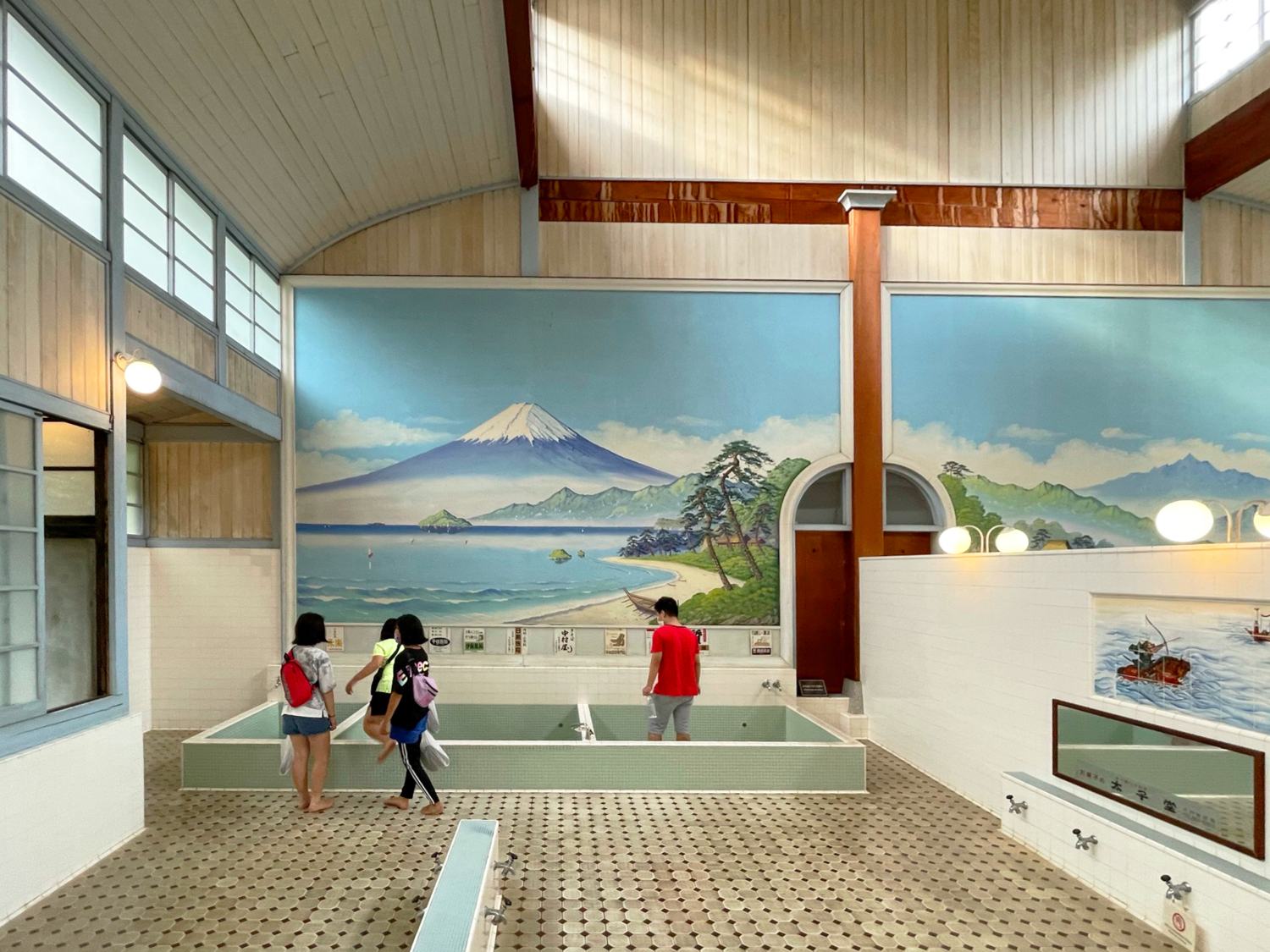 The men's bath at a Japanese sento, a tiled pool under a painted mural of Mount Fuji.