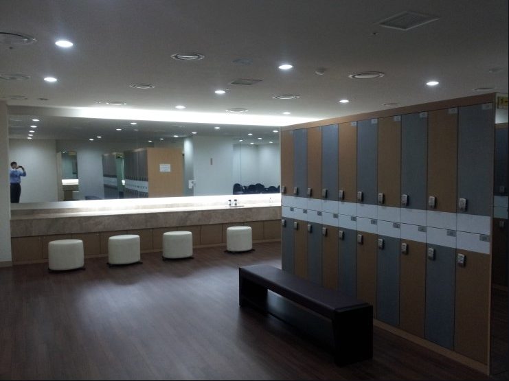 A sauna locker room in a Seoul apartment-hotel, 2015: light wood lockers, a long counter with mirrors, white stools.