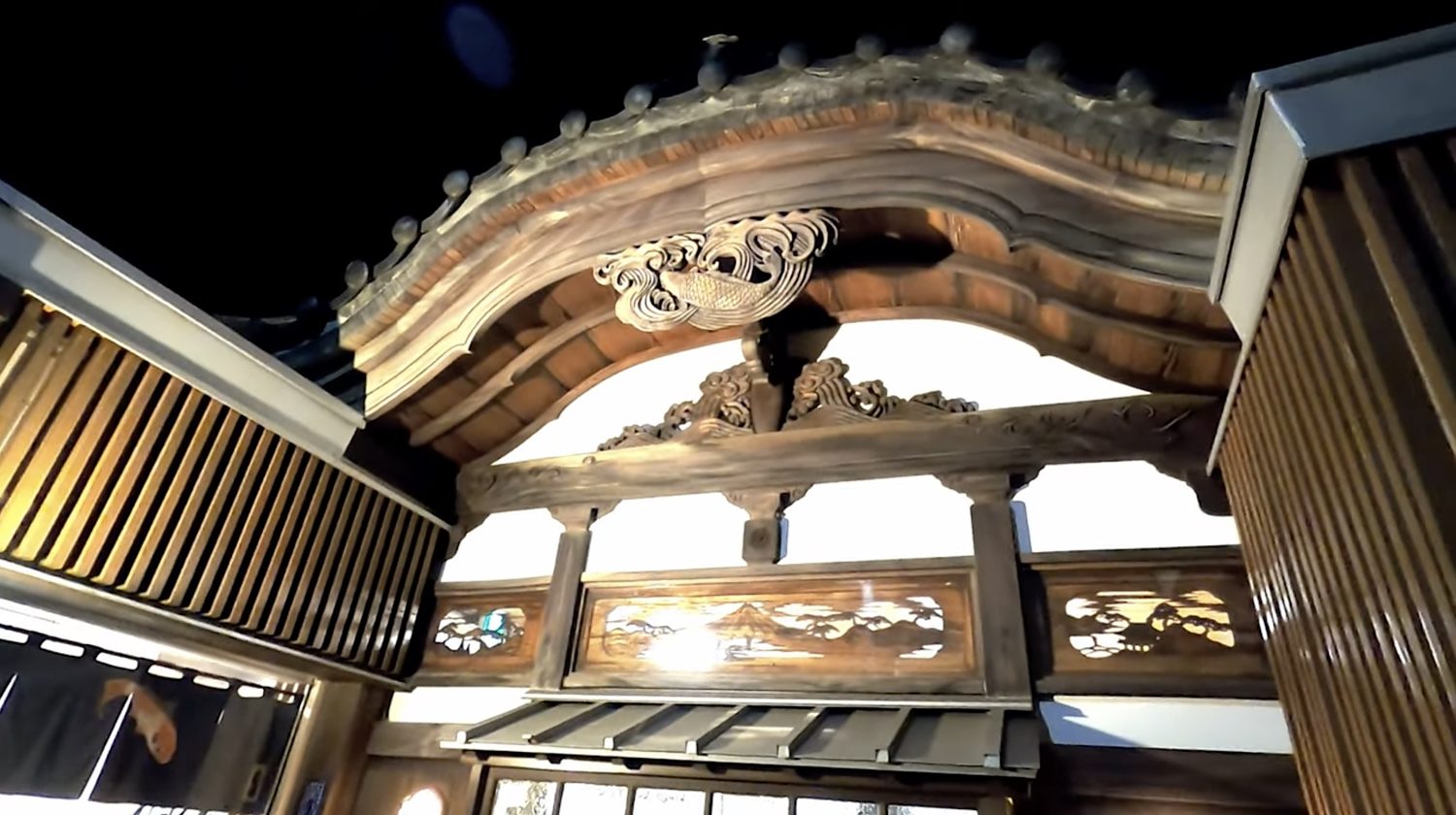 The street front of Kosugiyu, a 1933 bathhouse in Koenji, Tokyo, with its curved tiled roof and carved wooden gable.
