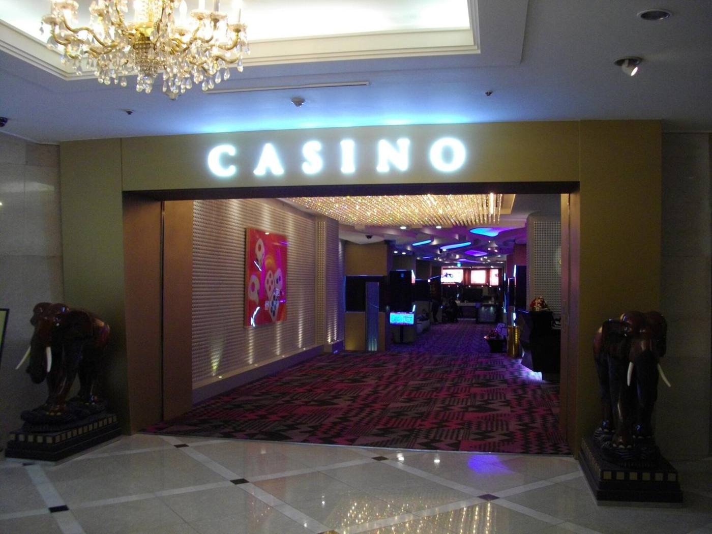 The entrance of Paradise Casino Jeju Grand: a gold-walled doorway flanked by two carved elephant statues, with a lit CASINO sign and patterned carpet beyond.